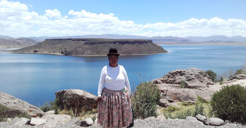 Mujer del altiplano en el complejo arqueológico, de fondo la laguna Umayo experiencia en el tour chullpas de Sillustani.